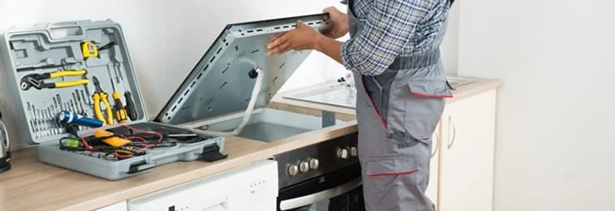 Cooktop repair technician lifting a built-in stovetop for service in Charlotte, NC