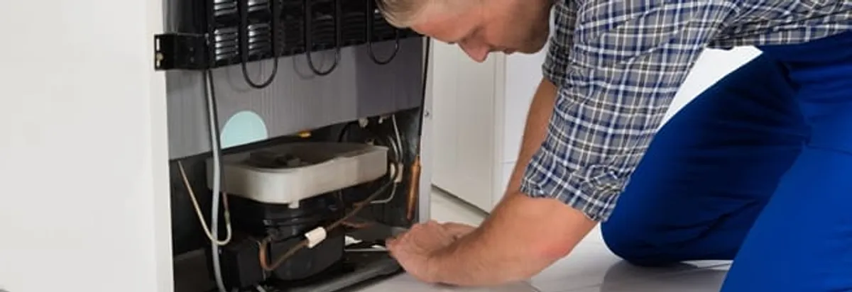 Refrigerator repair technician servicing the compressor and condenser area in Charlotte, NC