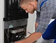 Refrigerator repair technician servicing the compressor and condenser area in Charlotte, NC